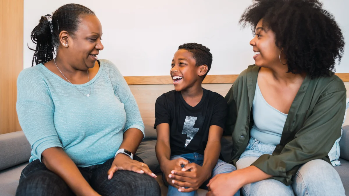 Two women and a young boy laughing together on a sofa indoors