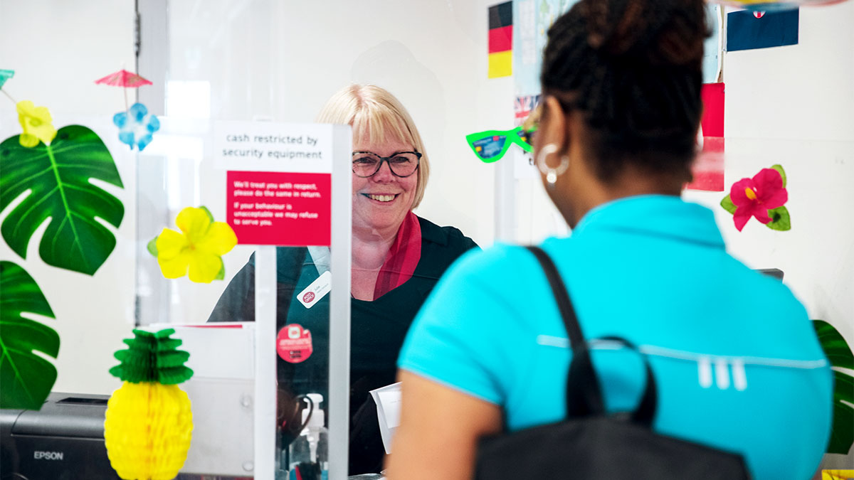 Female customer at a Post Office branch counter with a female member of counter staff smiling back