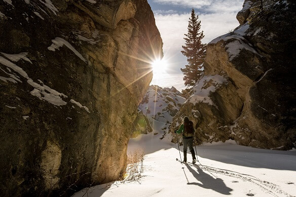 Cross-country skier on snowy path in mountain terrain beneath a sunny sky