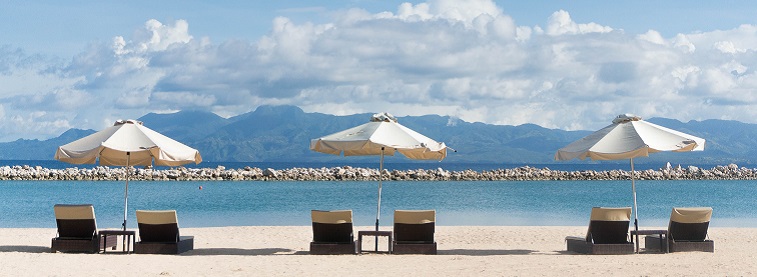 Sun loungers and parasols on sandy beach pointing toward the sea and distant mountains