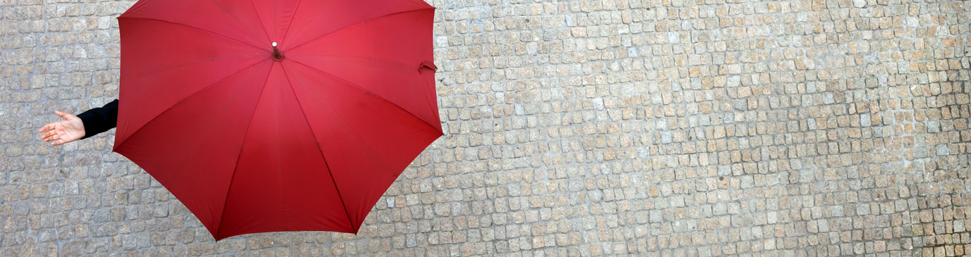 Person on cobble street under an open red umbrella holding their hand out to feel the rain