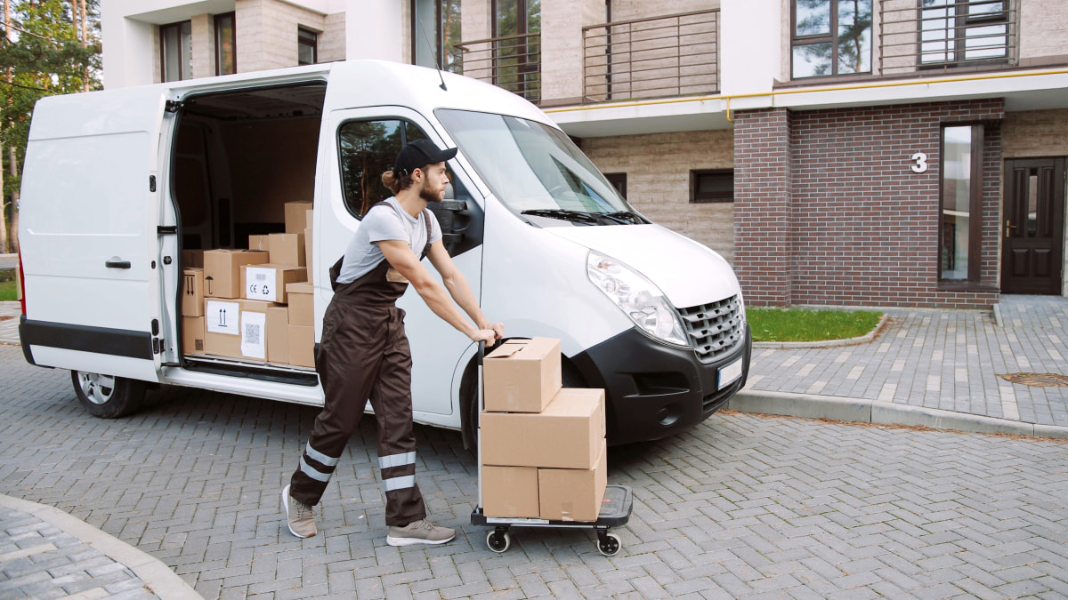 Delivery driver beside a van pushing a wheeled stack of boxes to be delivered to various addresses