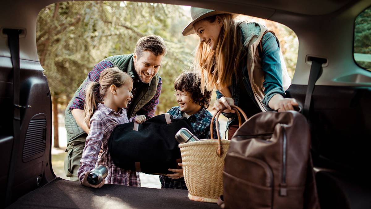 a happy family of four loading a car with picnic essentials