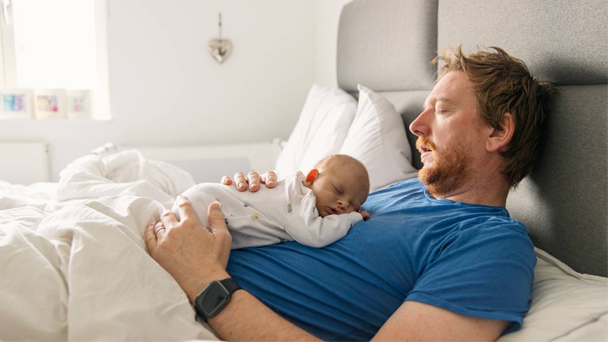 a man snoozing on a bed with a newborn baby resting on his chest