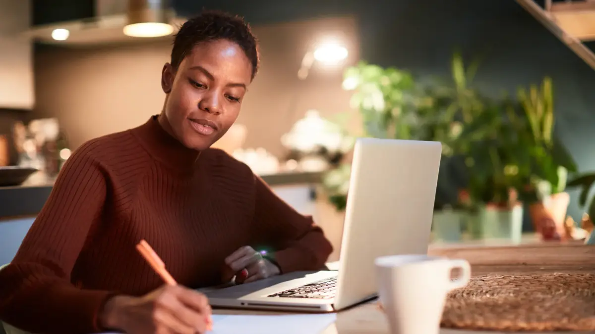a person seated at a laptop and writing on paper