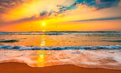 Beach with sea waves lapping on to beach and a beautiful sunset in the distance