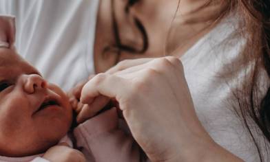 Baby girl in a pink outfit and matching headband, looking at her mum, holding her mum's hand