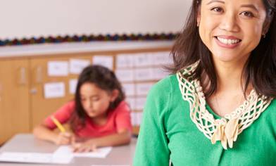 Smiling female teacher in green cardigan in foreground, child student writing in background