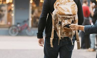 Man with rolled sleeve taking item from backpack on another man walking in ahead in a street