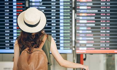 Woman wearing hat and backpack at airport looking a departure board at the airport