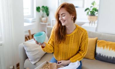 A person sitting on a sofa at home, unpacking a light blue mug from a delivery box
