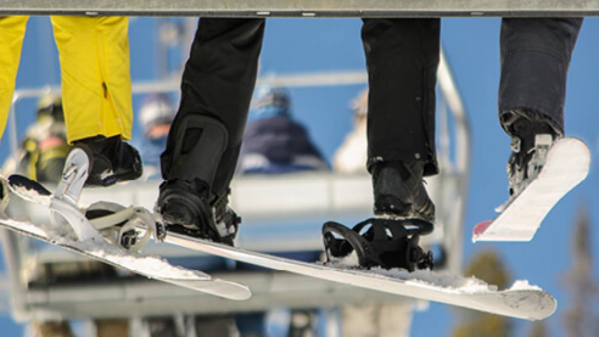 Skier legs and boots in skis on a ski lift with other ski lifts with skiers in them in background