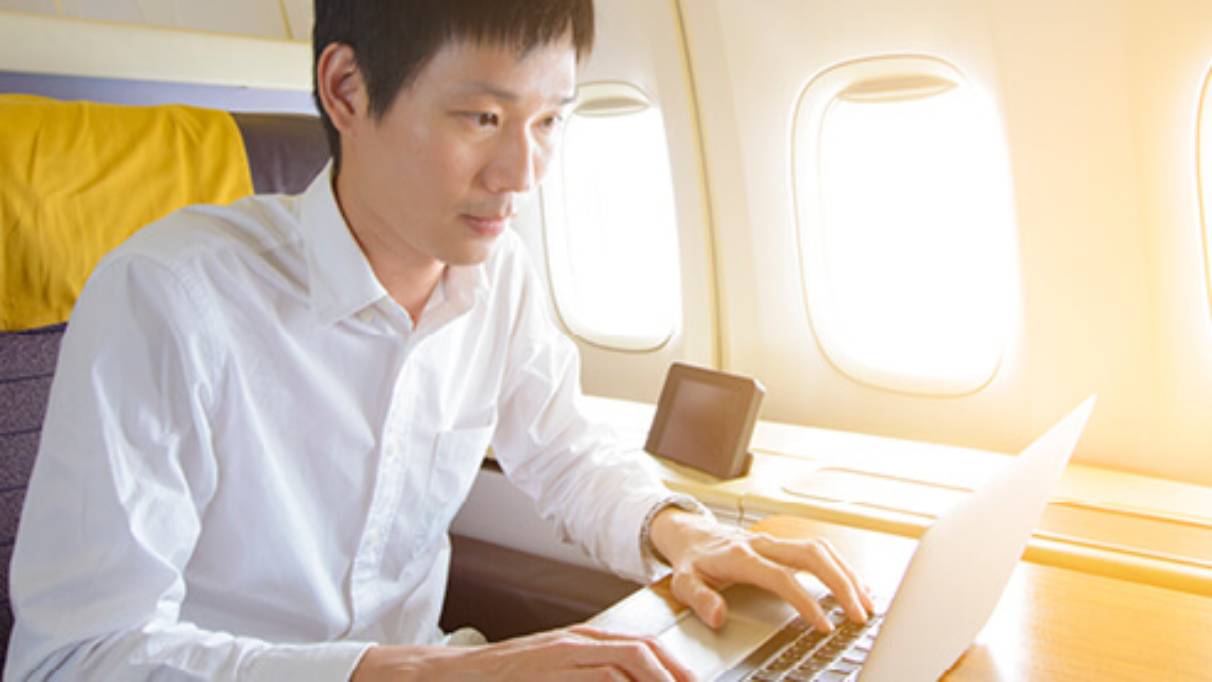 Man on plane in upgraded seating working on his laptop