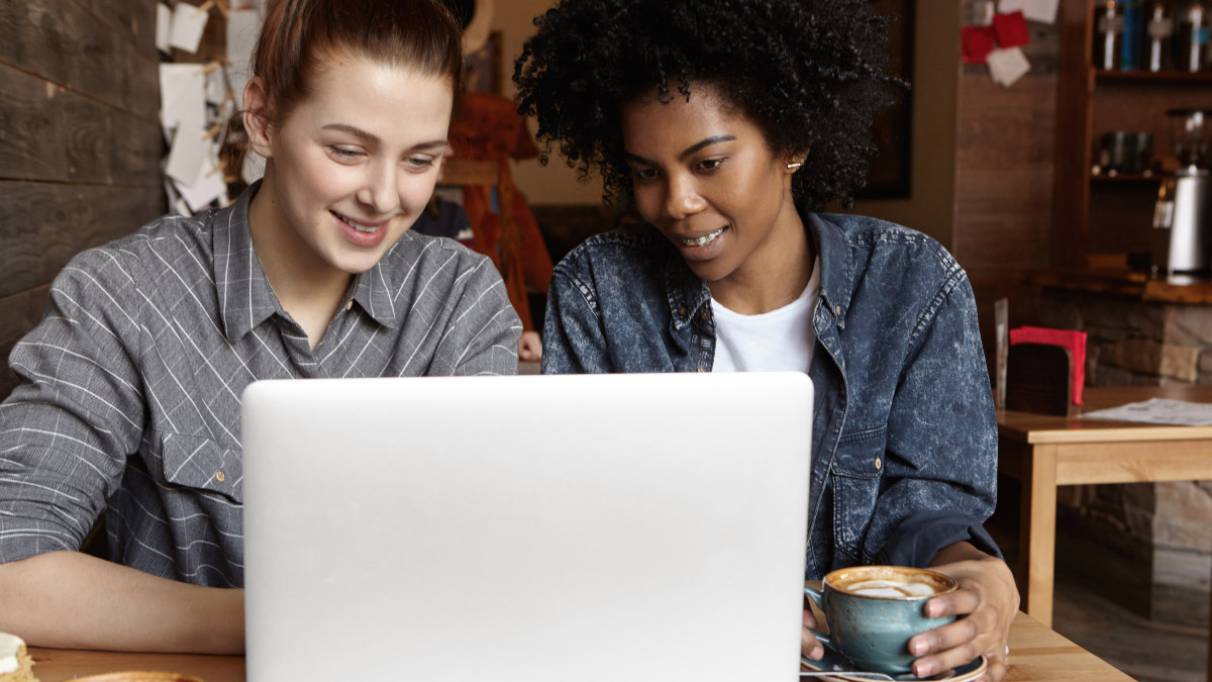Two female students working on common university project using laptop computer together at cafe 
