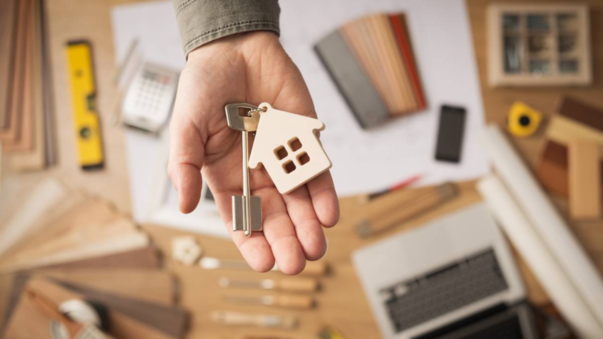 Key with metal house keyring attached, resting inside the palm of a hand above a work bench