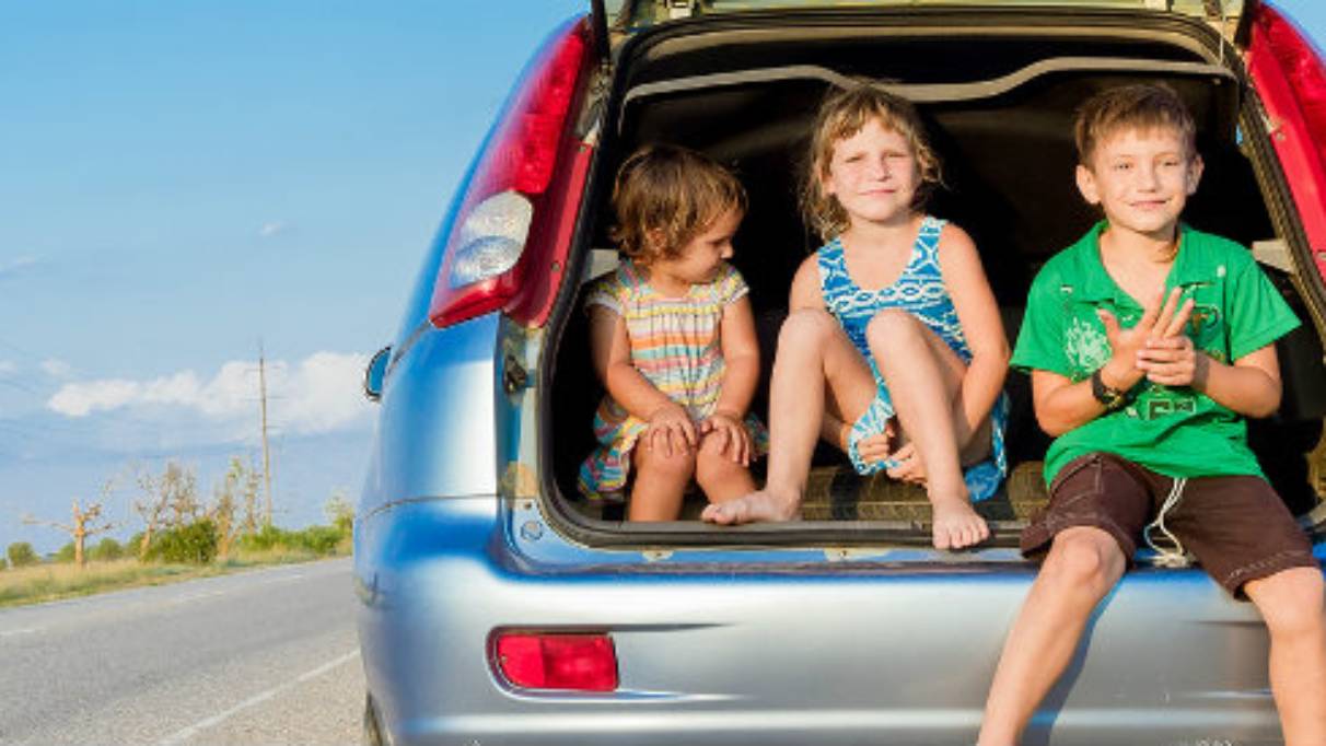 Three happy smiling kids sitting in the back of a car