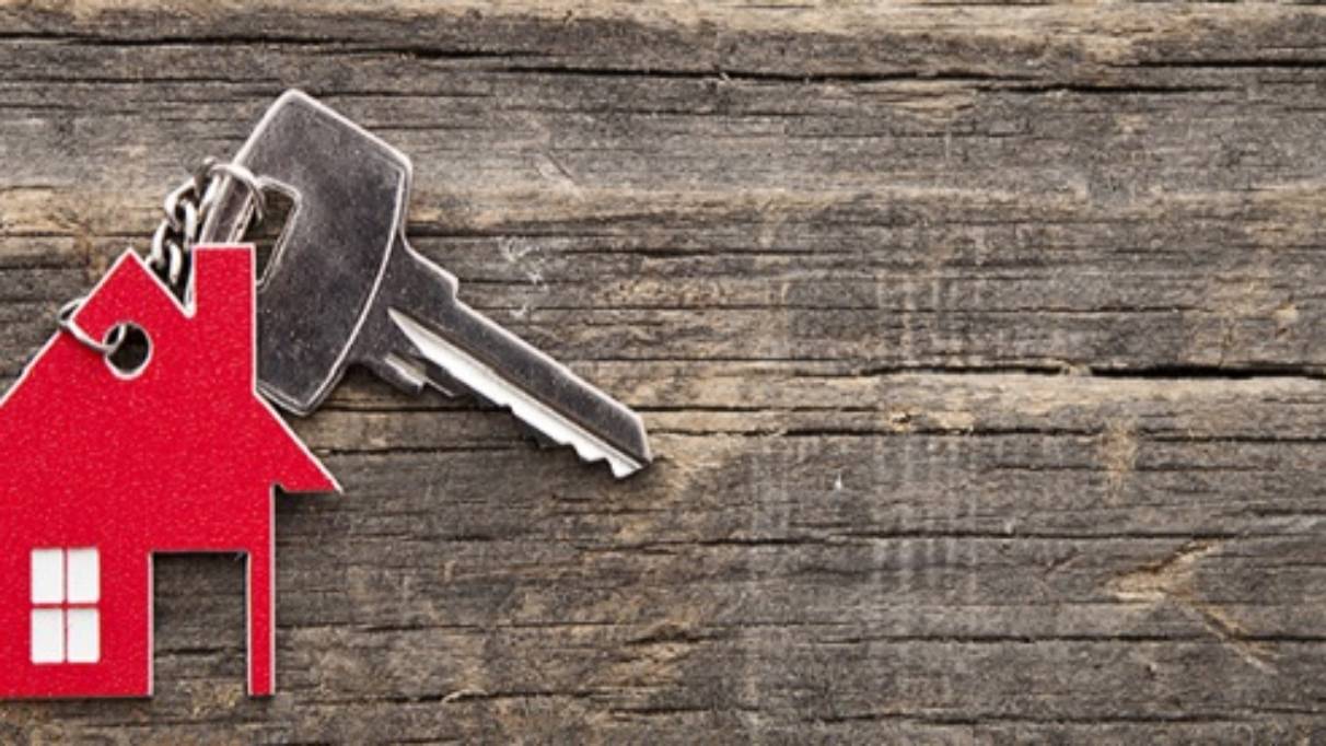 Key with red house key ring attached with chain laying on wooden surface