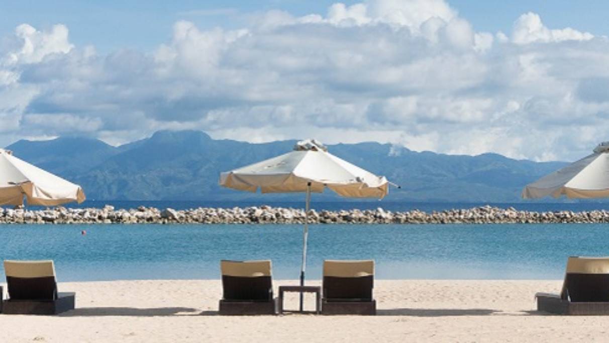 Sun loungers and parasols on sandy beach pointing toward the sea and distant mountains