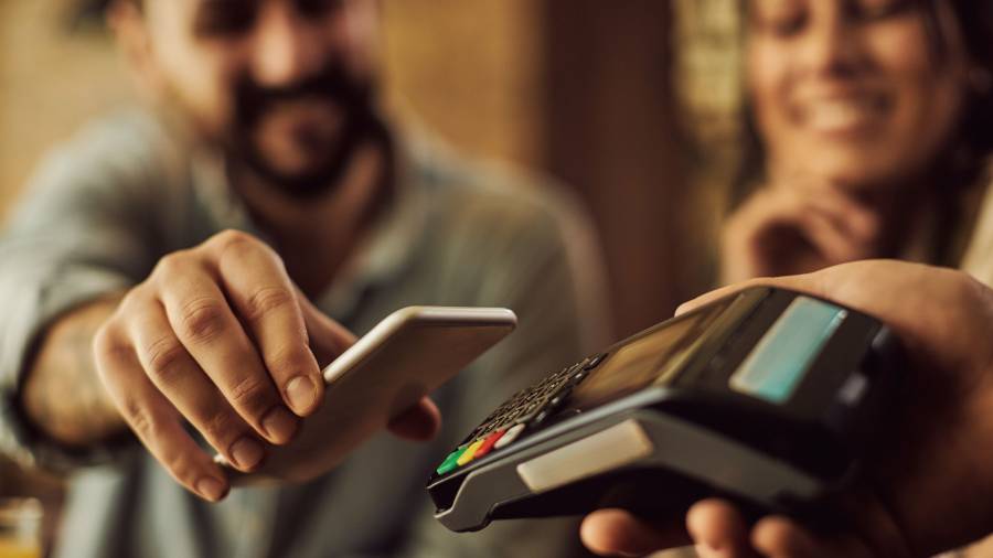 A person holding a phone up to a credit card reader. Another person sits next to them smiling 
