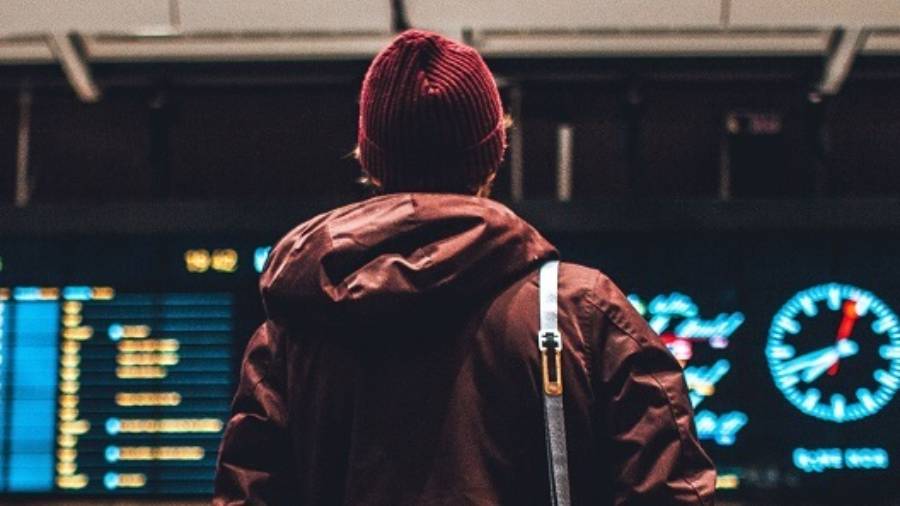 Male wearing beanie and winter jacket looking up at departures boards at the airport
