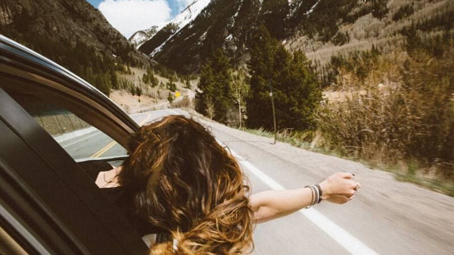 Car driving down winding mountainous road with woman leaning her head and arm out of passenger window