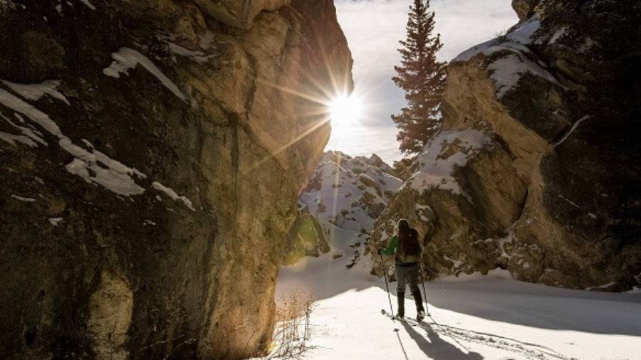 Cross-country skier on snowy path in mountain terrain beneath a sunny sky