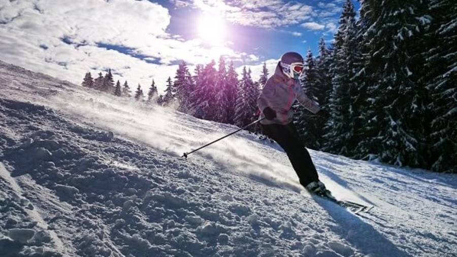 Skier wearing helmet and goggles skiing with snow spray behind and trees in background