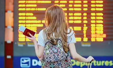 young lady checking the flight times on the board whilst holding her passport