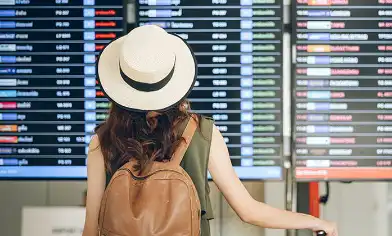 Woman wearing hat and backpack at airport looking a departure board at the airport