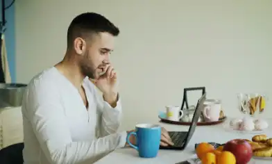 A person sitting at a table on the phone with a laptop and blue mug