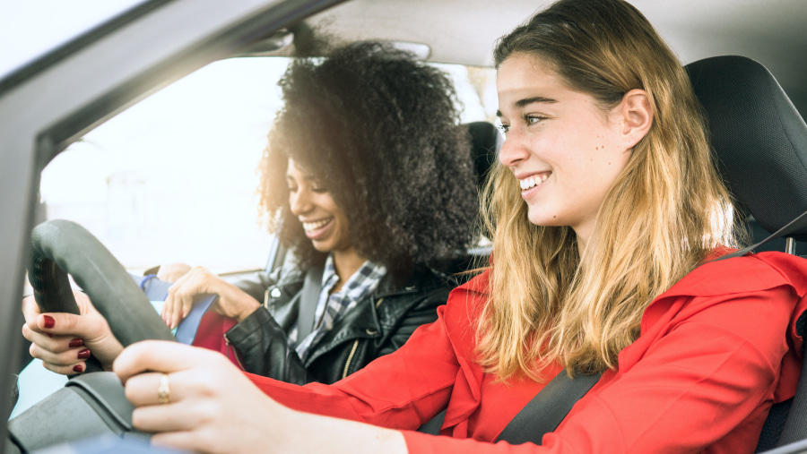 Two women in a car, in foreground in a red top is the driver, in the distance is the passenger