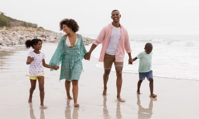 Young family of four walking along a sandy beach with waves to their left